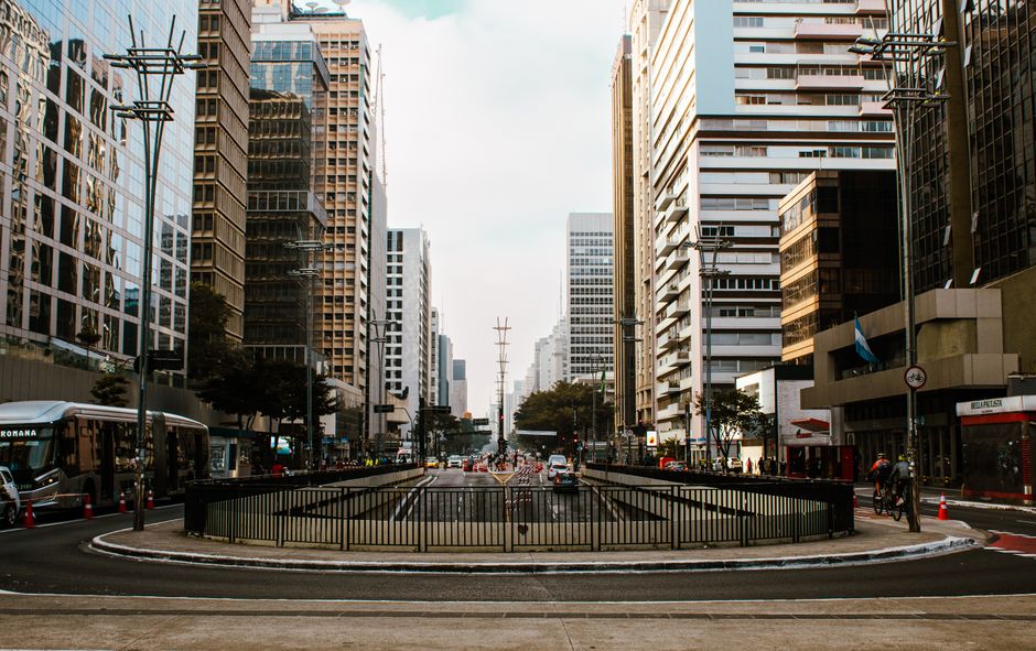 Vista de uma rua urbana movimentada cercada por arranha-céus e trânsito, transmitindo o ambiente de negócios e vida na cidade.