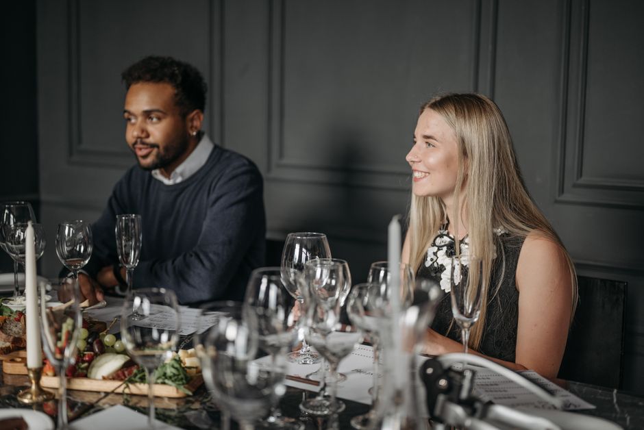 Homens e mulheres desfrutando de uma reunião ou jantar em um ambiente elegante, com foco na interação social e convivência formal.