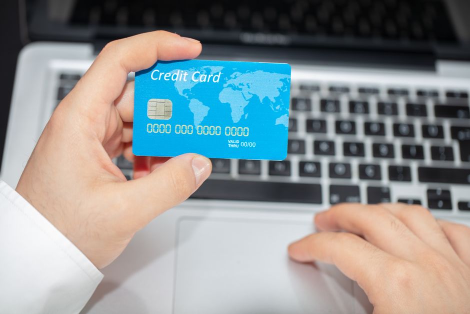 Pessoa segurando um cartão de crédito com um laptop aberto ao fundo, simbolizando temas de financiamento ou compras online.