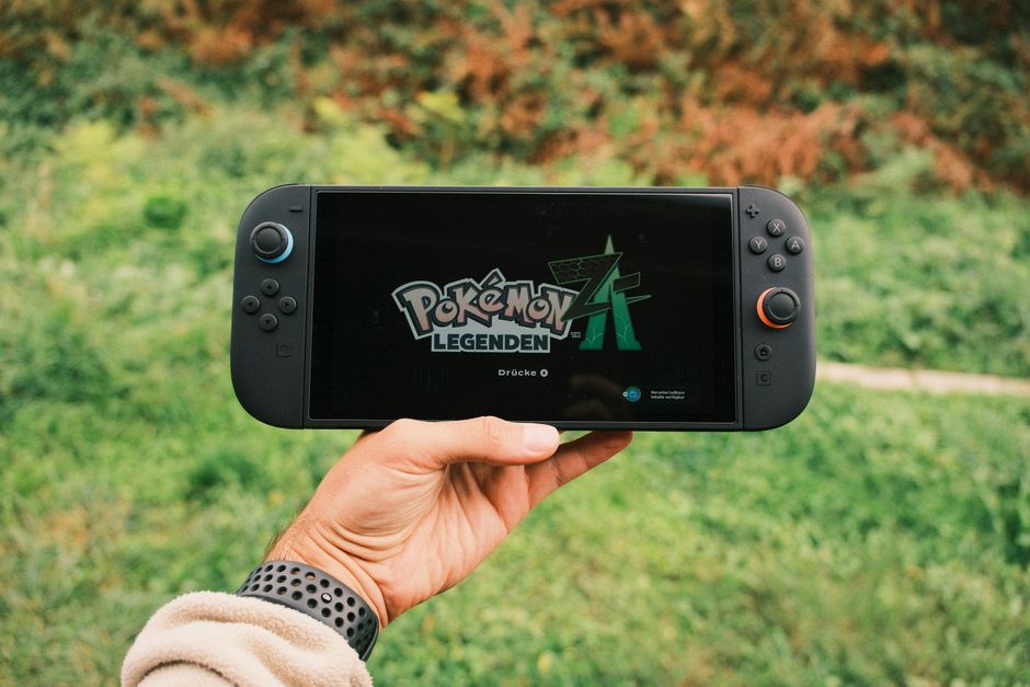 Pessoa segurando um console portátil de jogos com o logo de Pokémon Legends em um ambiente ao ar livre, destacando o tema de jogos e entretenimento digital.