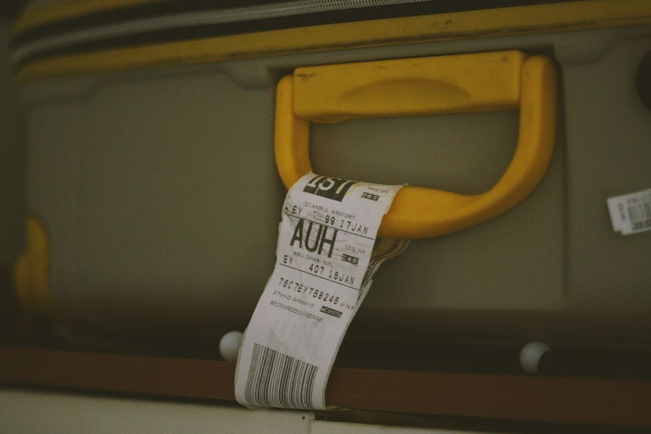 Imagem de uma cabine de embarque de aeroporto com uma etiqueta de passagem aérea pendurada no puxador de uma mala, representando viagens e planejamento de deslocamentos internacionais.