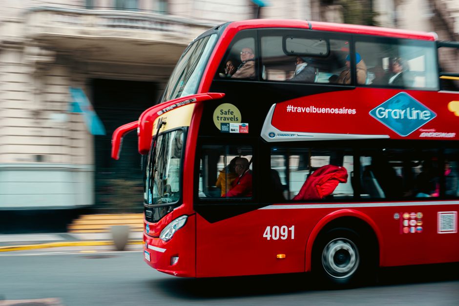Imagem de um ônibus de dois andares vermelho em movimento pelas ruas de Buenos Aires, simbolizando transporte urbano e mobilidade na cidade.