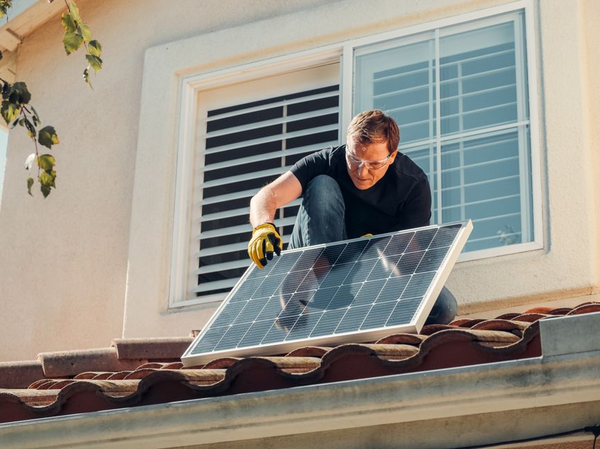 Homem instalando painel solar no telhado de uma residência, demonstrando sustentabilidade e energia renovável.