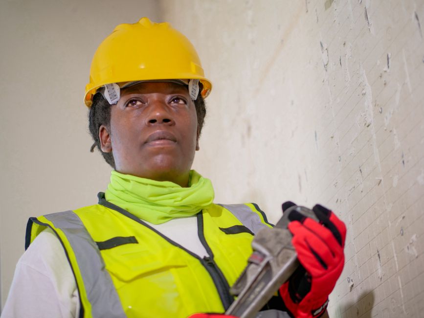 Profissional de construção civil com capacete e colete de segurança, demonstrando foco e determinação durante o trabalho na obra.