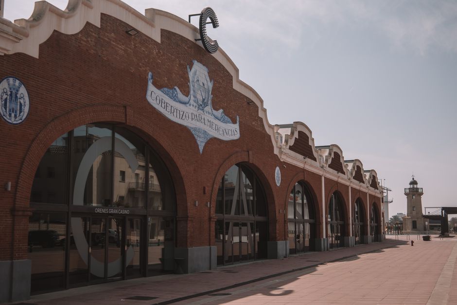 Imagem de um antigo edifício de arquitetura história, localizado na orla de uma cidade portuária, com destaque para sua fachada de tijolos e detalhes arquitetônicos clássicos.