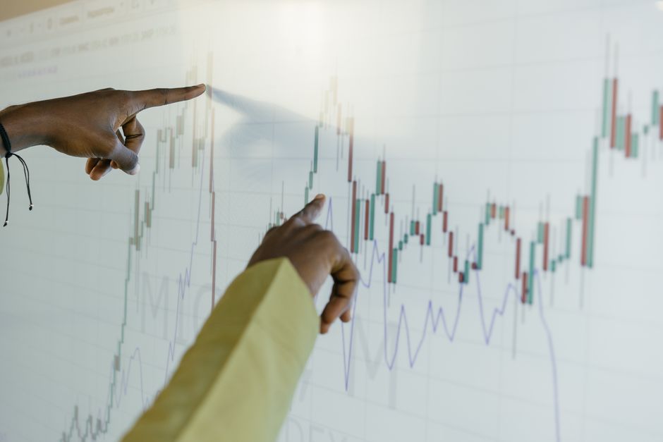 Dupla analisando gráficos de mercado financeiro durante uma apresentação de estratégias de investimento.