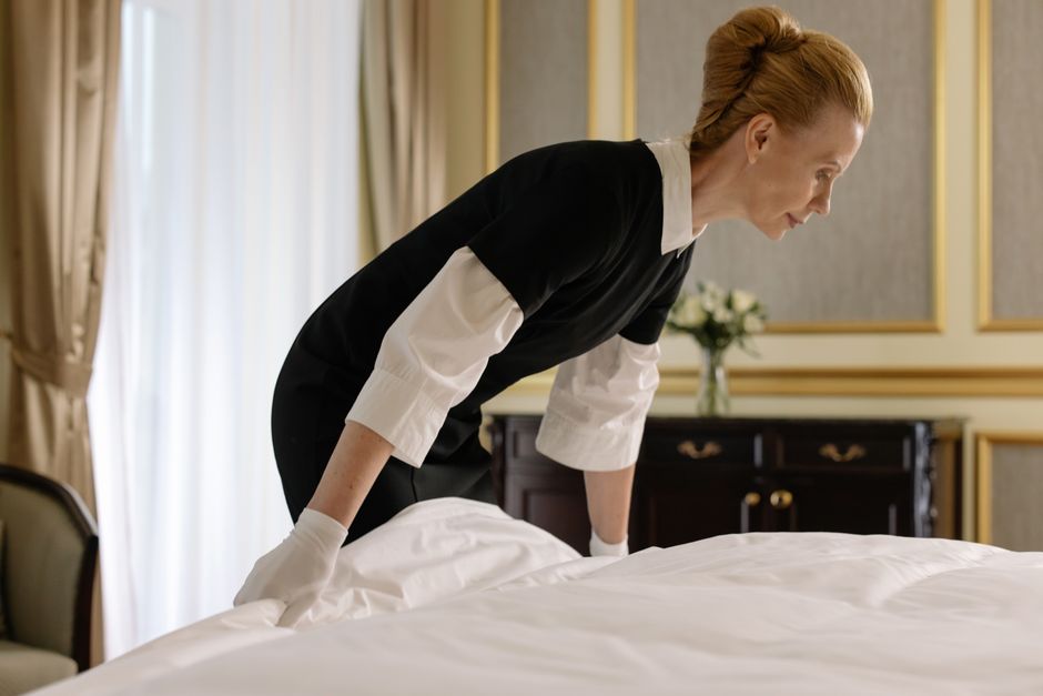 Mulher arrumando a cama em ambiente elegante, transmitindo cuidado e atenção ao ambiente doméstico ou de hospedagem.