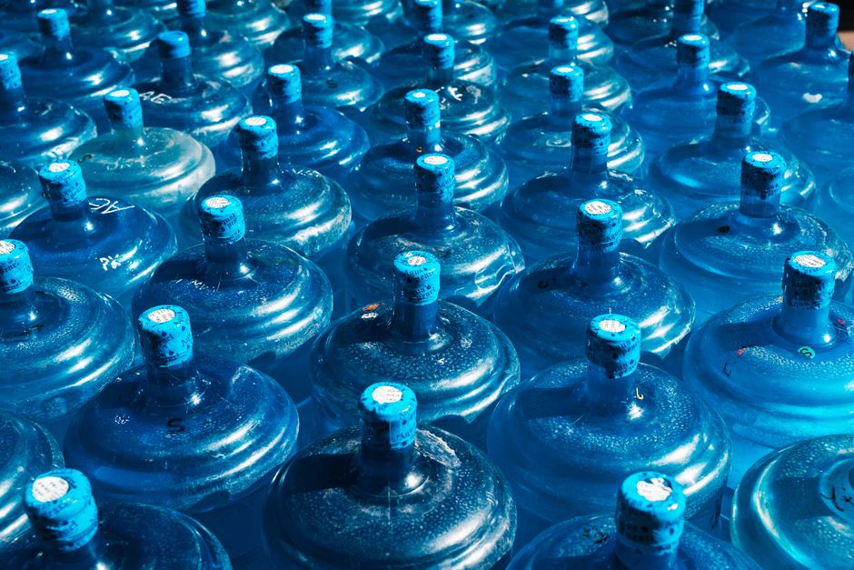 Imagem de várias garrafas de água mineral empilhadas, refletindo luz em tom azul, remetendo à hidratação e cuidados com a saúde.