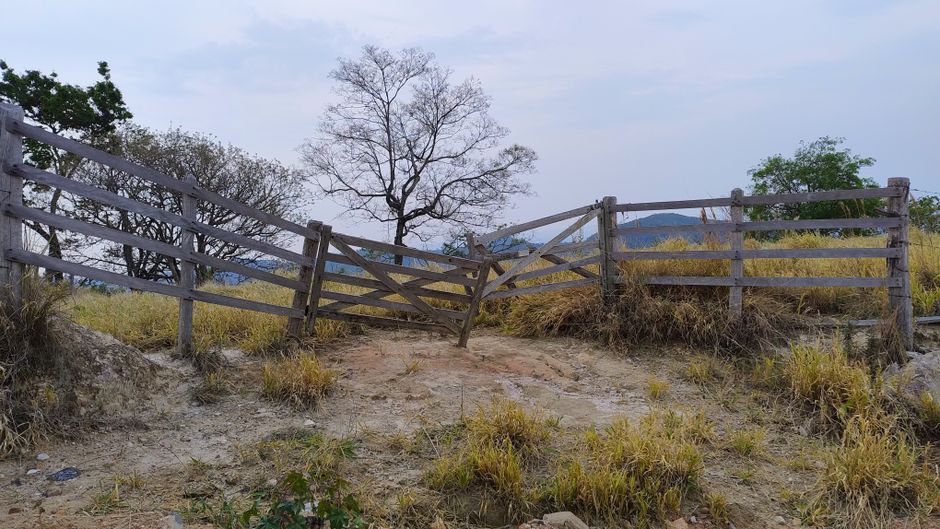 Imagem de uma cerca de madeira inclinada e danificada em um ambiente rural, simbolizando obstáculos ou abandono na paisagem natural.