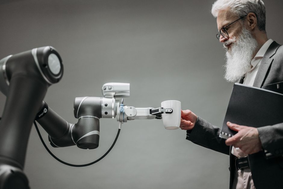 Homem de terno, com barba e óculos, interagindo com um robô que entrega uma xícara de café, destacando inovação e tecnologia no ambiente corporativo.