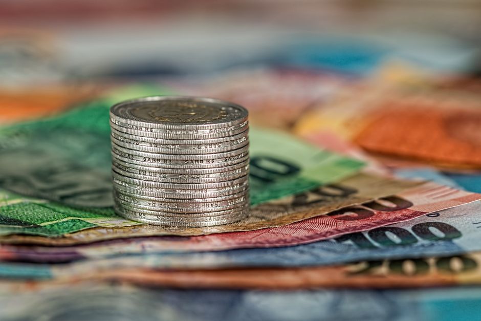 Imagem de uma pilha de moedas sobre várias cédulas de dinheiro brasileiras, simbolizando finanças e economia.