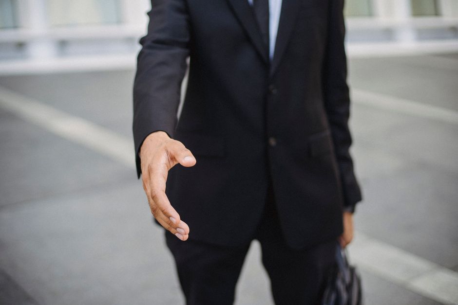 Homem de terno estendendo a mão para um aperto, simbolizando cumprimento ou oportunidade profissional.