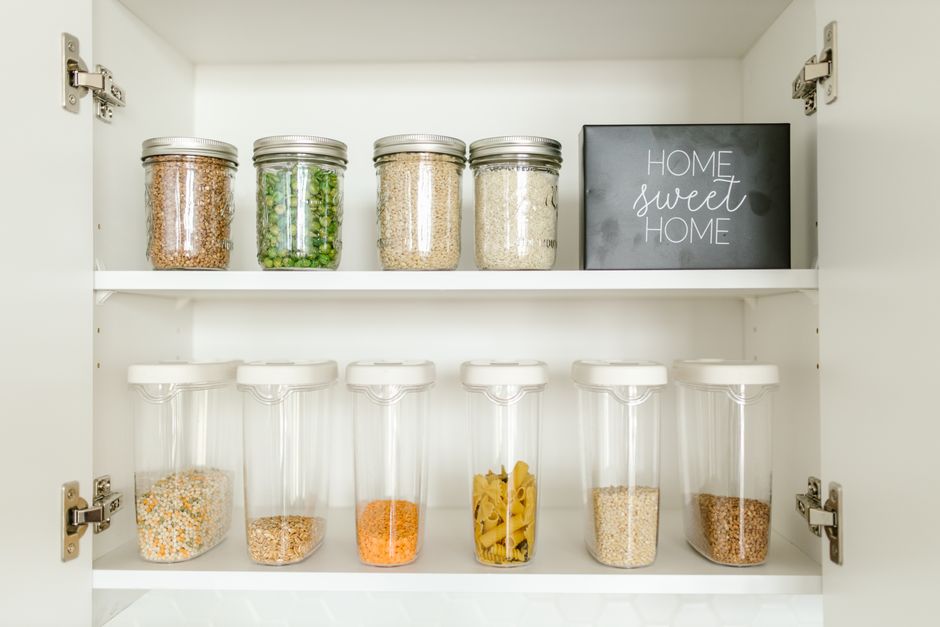 Armário de cozinha organizado com potes de ingredientes securos e uma placa decorativa que diz 'Home sweet home', transmitindo aconchego e organização doméstica.