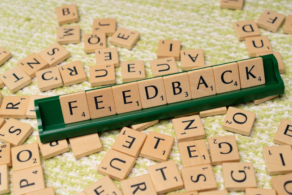 Imagem de blocos de letras formando a palavra 'feedback' sobre uma superfície, simbolizando comunicação e melhorias.