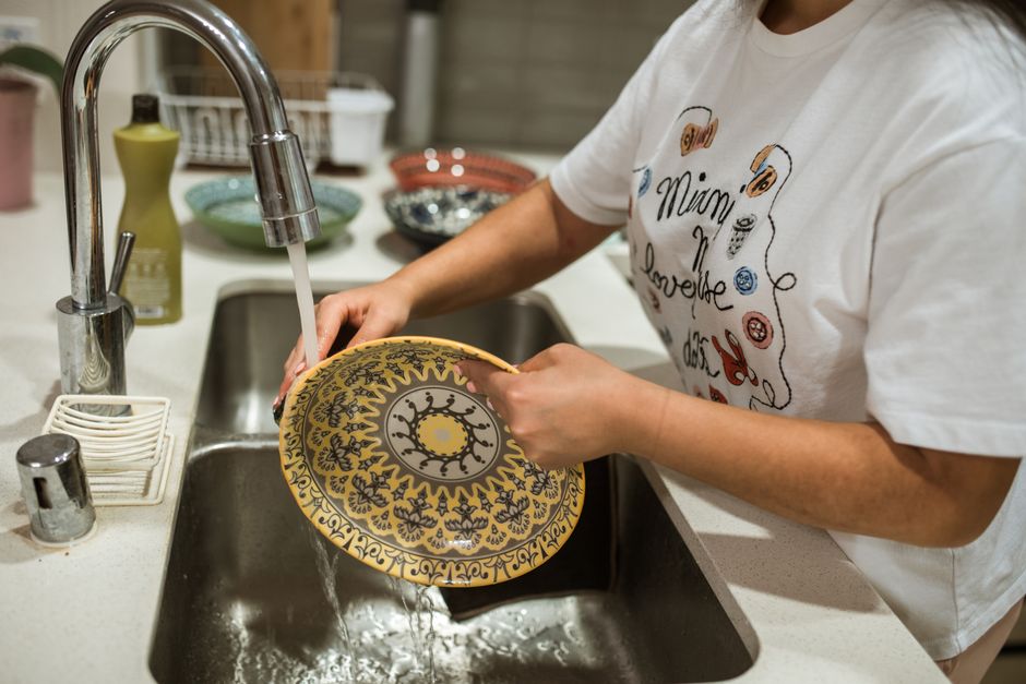 Pessoa lavando um prato decorado na cozinha, destacando o cuidado com a louça e o ambiente doméstico.