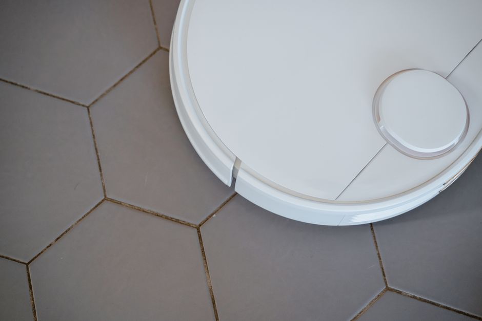 Imagem de um robô aspirador de pó em movimento no chão de azulejos, representando tecnologia doméstica e automação do lar.