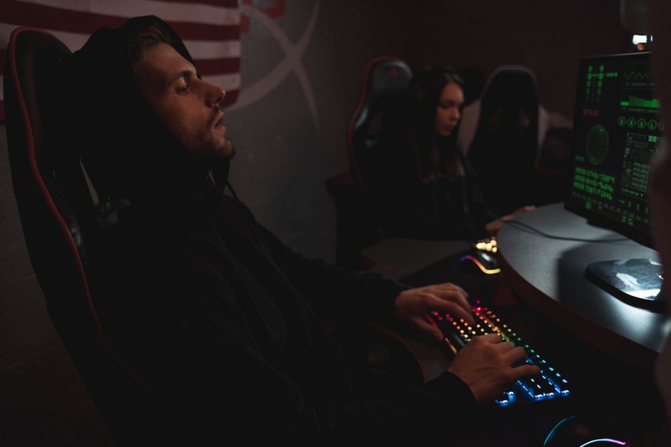 Pessoas jogando videogame em um ambiente escuro, com destaque para telas com gráficos digitais e iluminação de LED colorida.