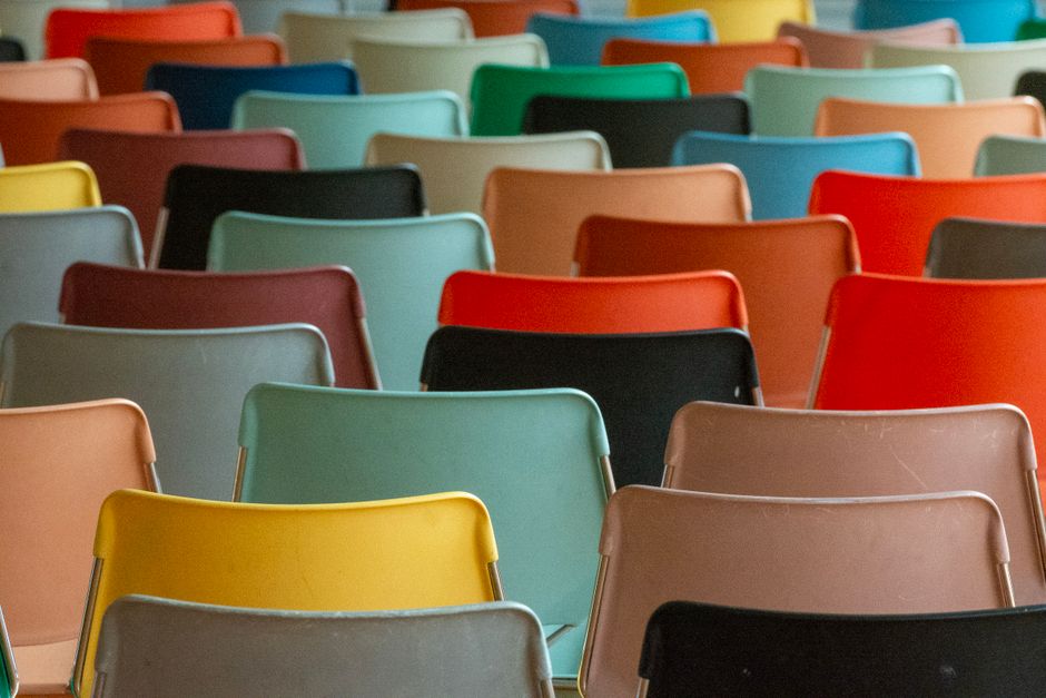 Filas de cadeiras coloridas em um ambiente de evento ou conferência, simbolizando participação e interação em uma sessão coletiva.