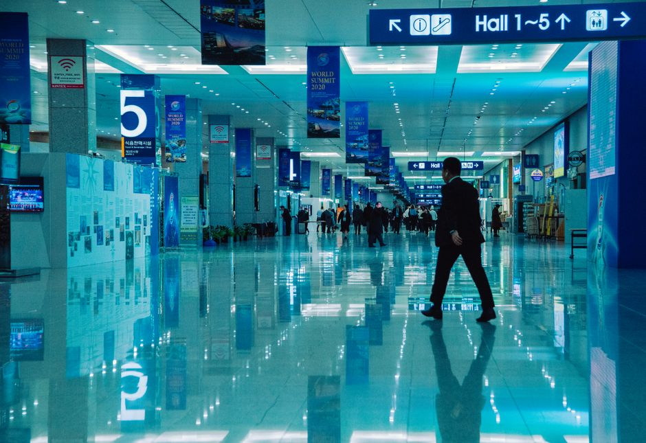 Imagem de um aeroporto movimentado com sinalização de destinos e pessoas caminhando pelo espaço, demonstrando o ambiente de viagens internacionais.