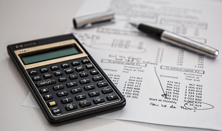 Imagem de uma calculadora, caneta e documentos financeiros sobre uma mesa, ilustrando análise e planejamento financeiro.