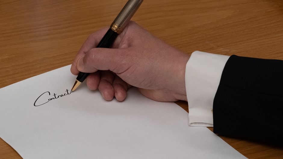Pessoa assinando um contrato em um ambiente de negócios formal, destacando a importância de acordos e parcerias empresariais.