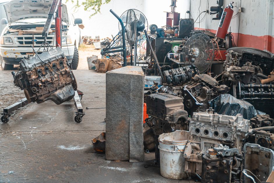 Ambiente de oficina ou espaço de trabalho com peças de motor, ferramentas e equipamentos mecânicos ao redor, sugerindo manutenção ou desmontagem de veículos.