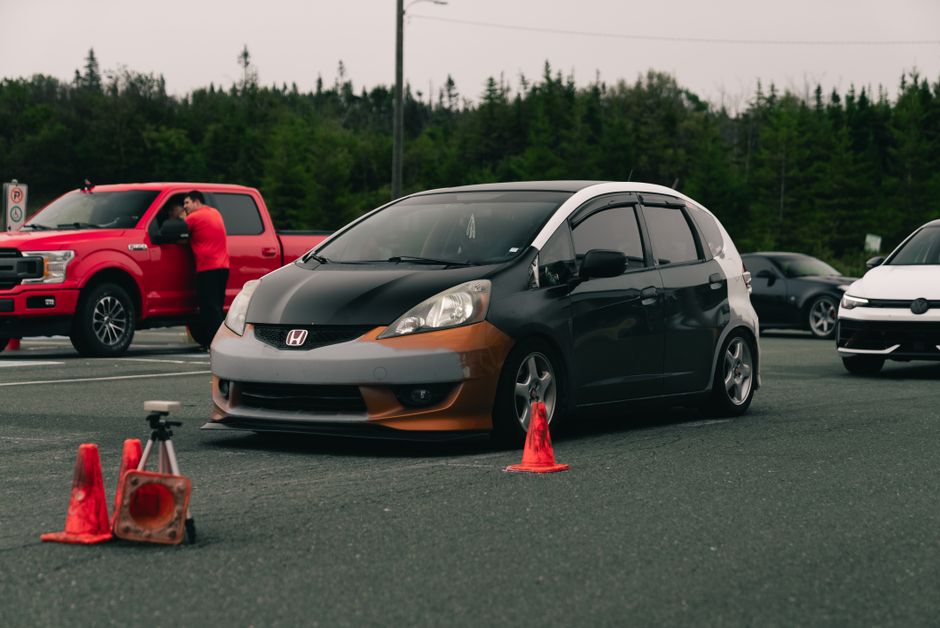 Carro compacto participando de um teste de segurança ou habilitação, com cones e equipamentos de medição ao redor, em uma pista ao ar livre.