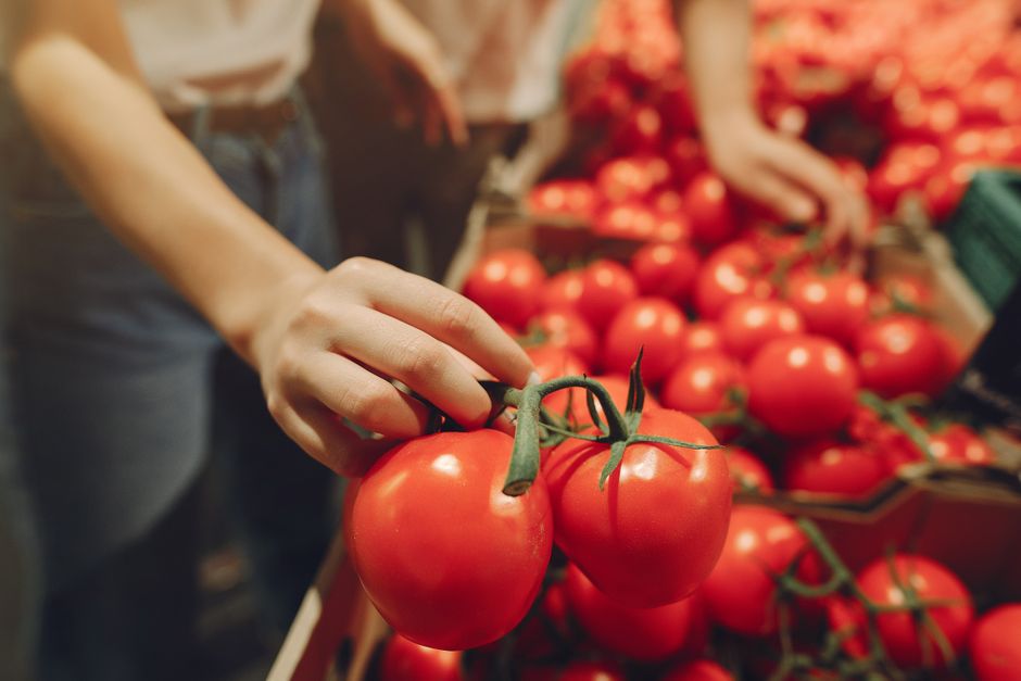 Pessoa escolhendo tomates frescos em uma feira ou hortifrúti, destacando a importância de alimentos naturais e saudáveis.