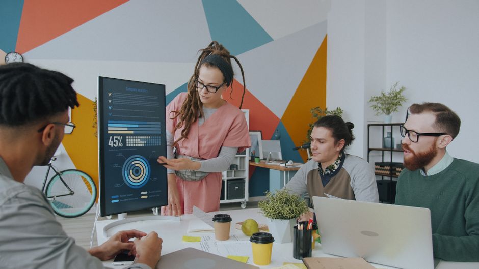 Equipe de profissionais de tecnologia analisando dados e apresentando gráficos em ambiente de escritório criativo.