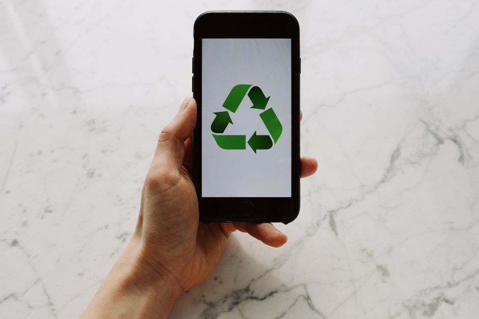 Pessoa segurando um smartphone exibindo símbolo de reciclagem, simbolizando sustentabilidade e consumo consciente.