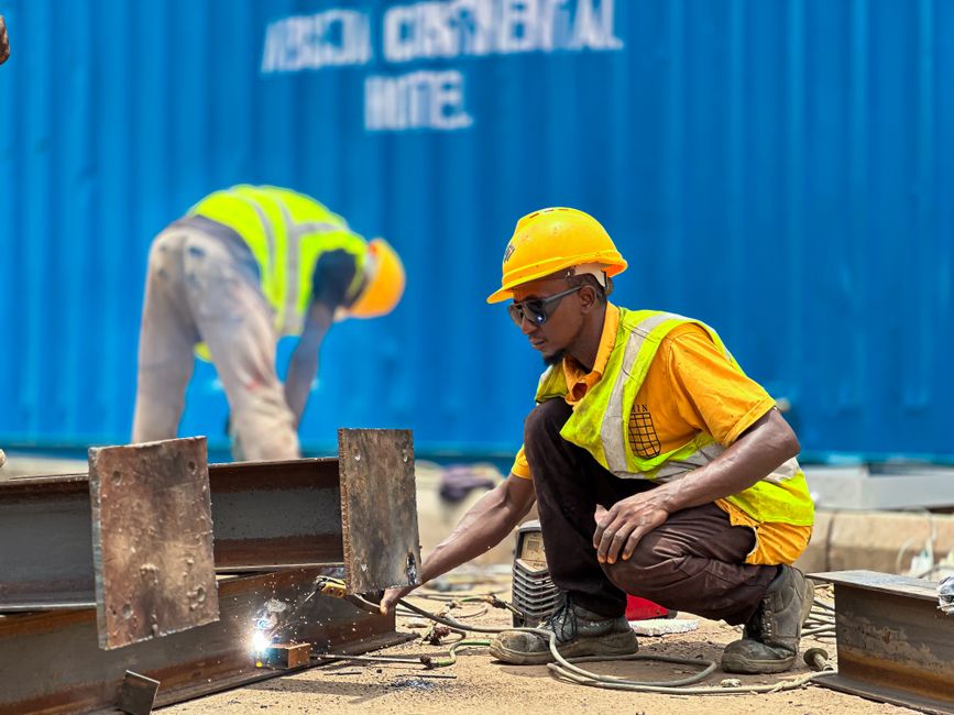 Foto de dois trabalhadores em um canteiro de obras utilizando equipamentos de proteção ao realizar soldagem, destacando a construção civil e segurança no trabalho.