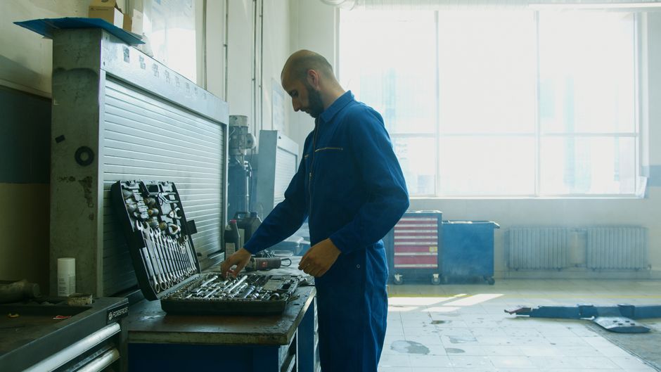 Imagem de um técnico de manutenção ajustando ferramentas em uma oficina industrial, destacando o ambiente de trabalho técnico e mecânico.
