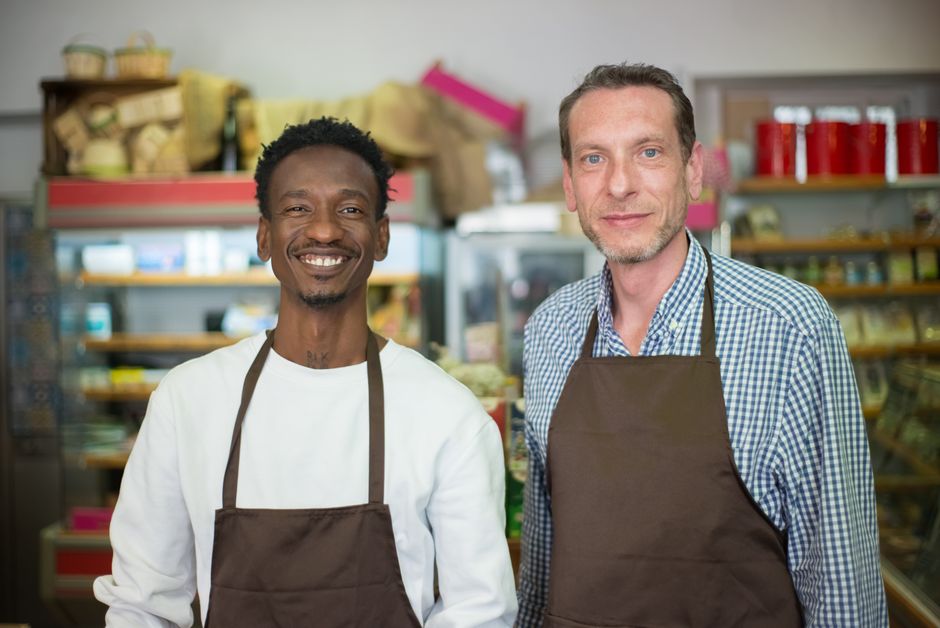 Dois homens sorridentes em uma loja de alimentos, representando empreendedorismo e comércio local.