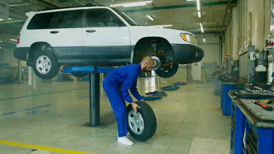 Mecânico trocando o pneu de um veículo elevado em uma oficina de manutenção automotiva.