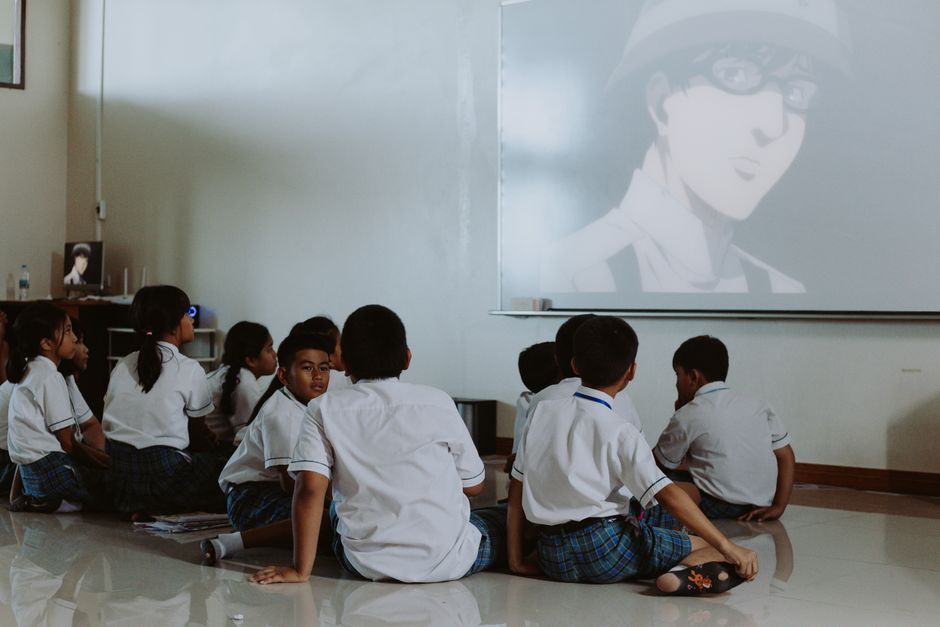 Crianças assistindo uma apresentação ou vídeo educativo na sala de aula, promovendo aprendizado e diversão.