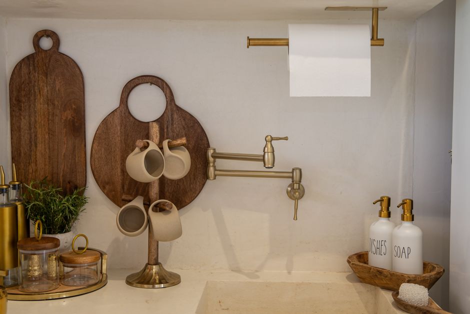 Imagem de uma área de cozinha com elementos decorativos em tons neutros, incluindo suportes para canecas, potes de papelaria e dispensadores de sabonete, criando um ambiente acolhedor e funcional.