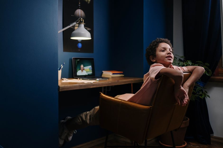 Um menino assistindo a uma videochamada ou aula online em um ambiente de home office, com expressão relaxada e confortável.