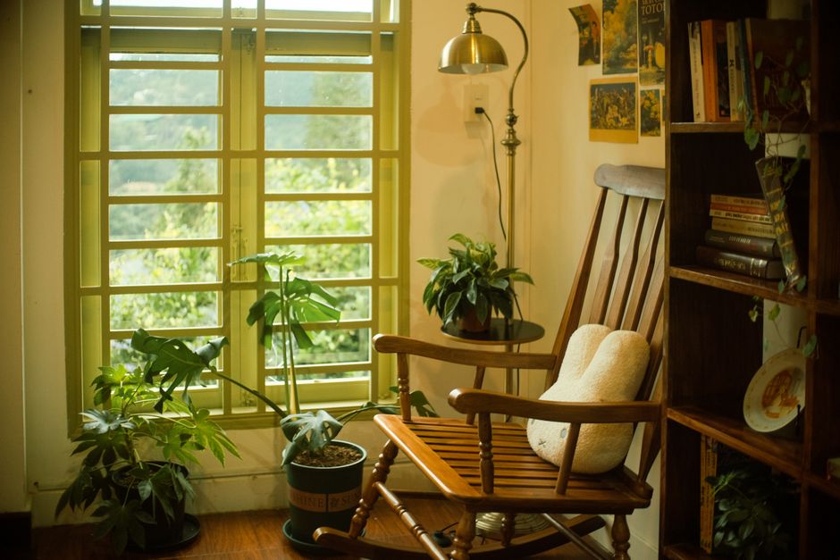 Sala aconchegante de leitura com cadeira de balanço, plantas e iluminação suave, ideal para relaxar e apreciar um bom livro.