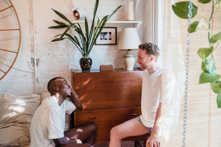 Dois homens conversando de forma amistosa em um ambiente aconchegante e decorado com plantas e objetos de decoração rústicos.