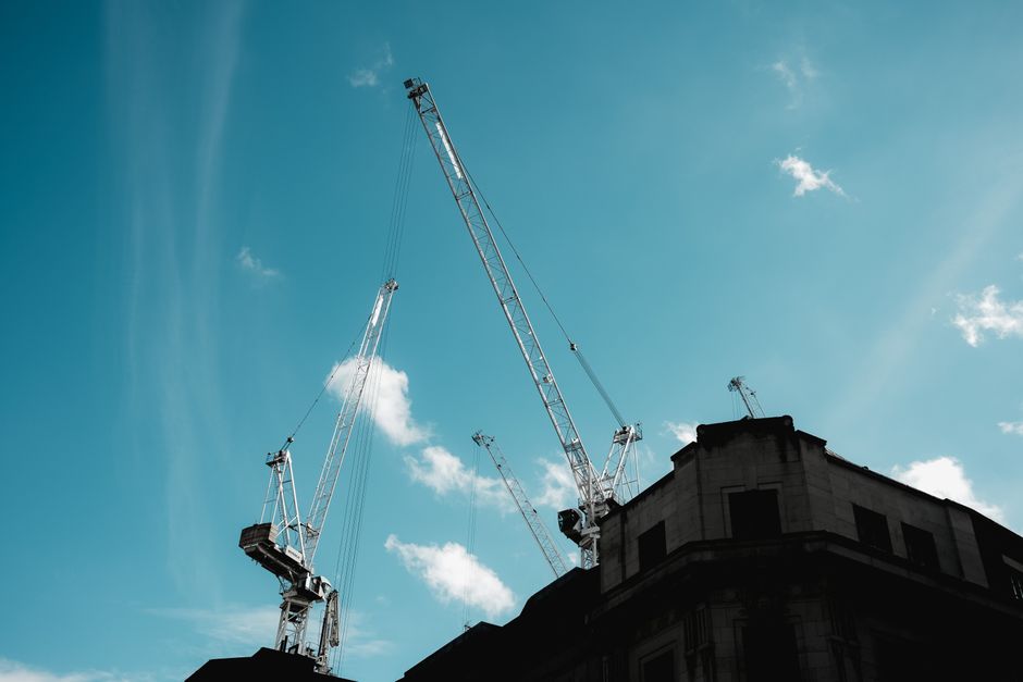 Imagem de edifício em construção com torres de guindaste sob céu claro, simbolizando desenvolvimento urbano e engenharia civil.