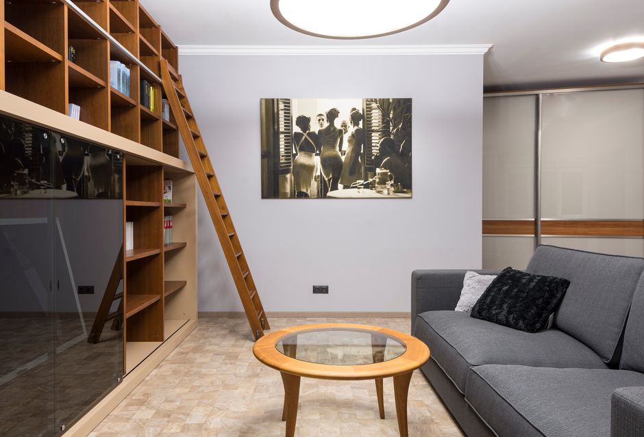Imagem de uma área de convivência moderna com estante de livros, sofá cinza e uma obra de arte em preto e branco na parede, ideal para artigos de blog sobre decoração de espaços de trabalho ou ambientes residenciais sofisticados.