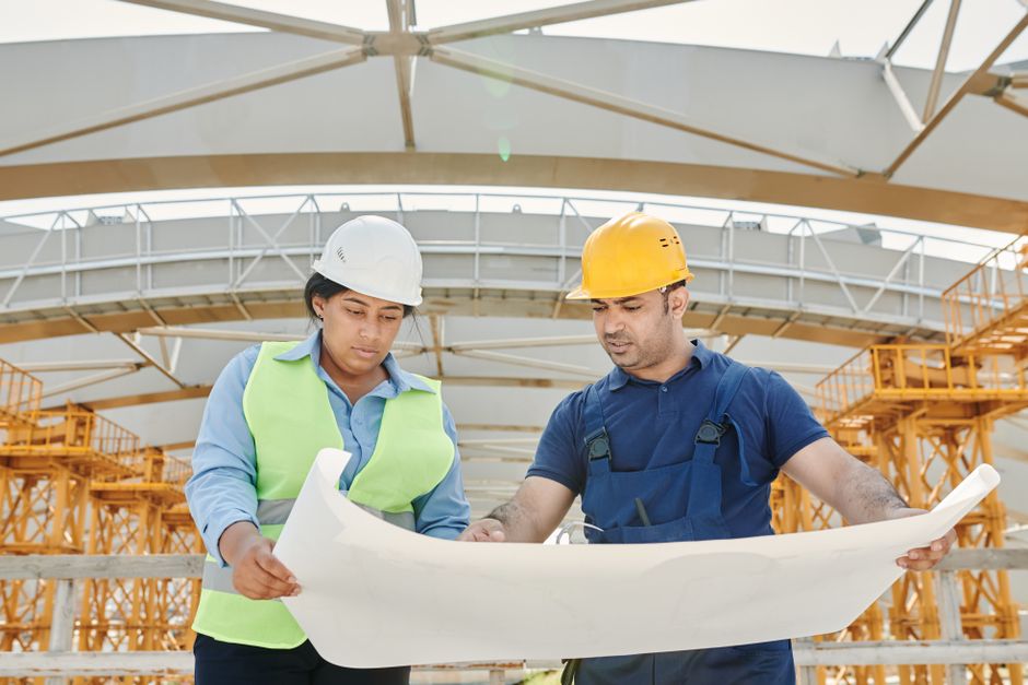 Engenheiros analisando planos de construção em um canteiro ao ar livre, simbolizando planejamento e supervisão de obras.