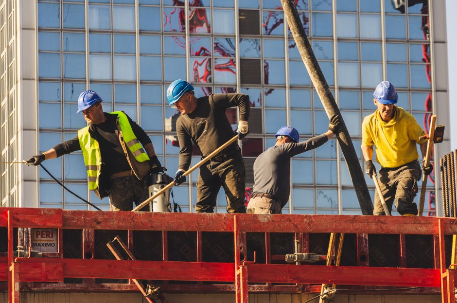 Equipe de trabalhadores da construção civil realizando tarefas de instalação em um edifício moderno com fachada de vidro.