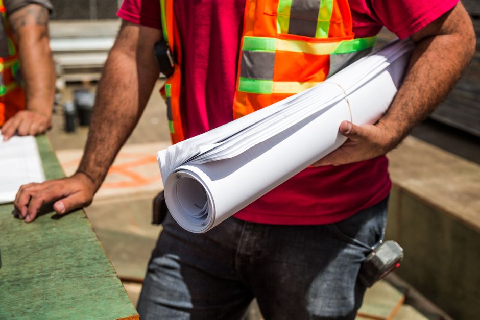 Profissional de construção civil segurando plantas e projetos em um ambiente de obra, representando planejamento e execução de obras.