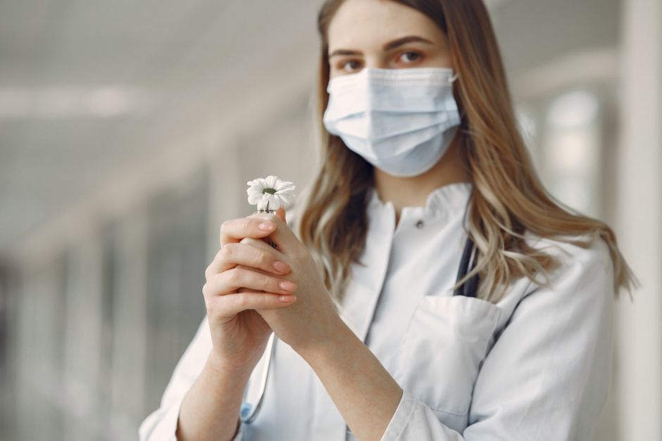Profissional de saúde com máscara, segurando uma flor, transmitindo esperança e cuidado em contexto de saúde.
