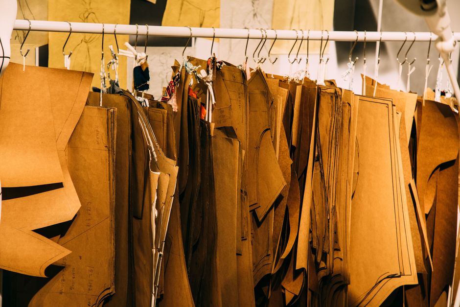 Pared de araras com moldes e papéis para confecção de roupas, representando criação e produção no setor de moda ou alfaiataria.