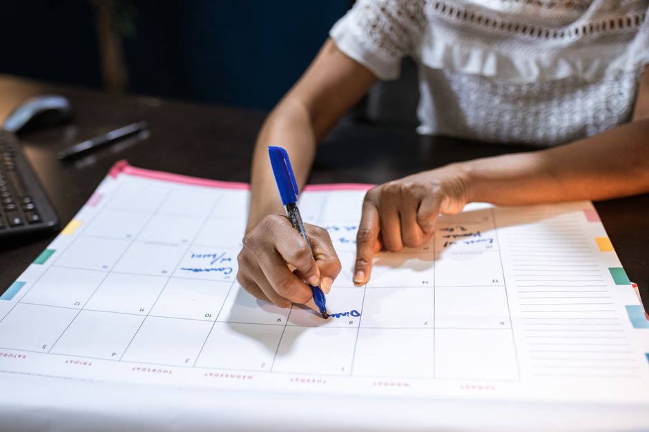 Pessoa organizando atividades e compromissos em um calendário mensal, representando planejamento e gestão de tempo.