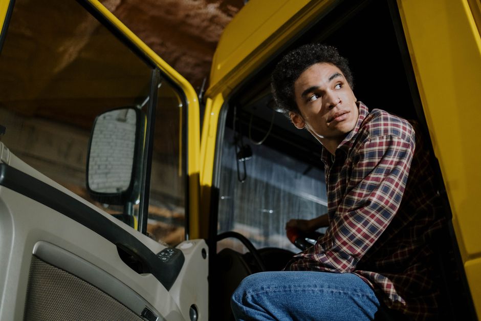 Jovem sentado dentro de um veículo de trabalho, demonstrando reflexão ou foco em ambientes industriais ou de transporte.