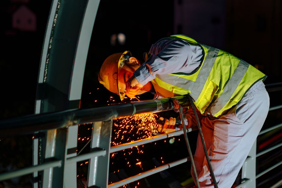 Imagem de um trabalhador soldador usando equipamentos de proteção ao realizar soldagem em obra industrial à noite.