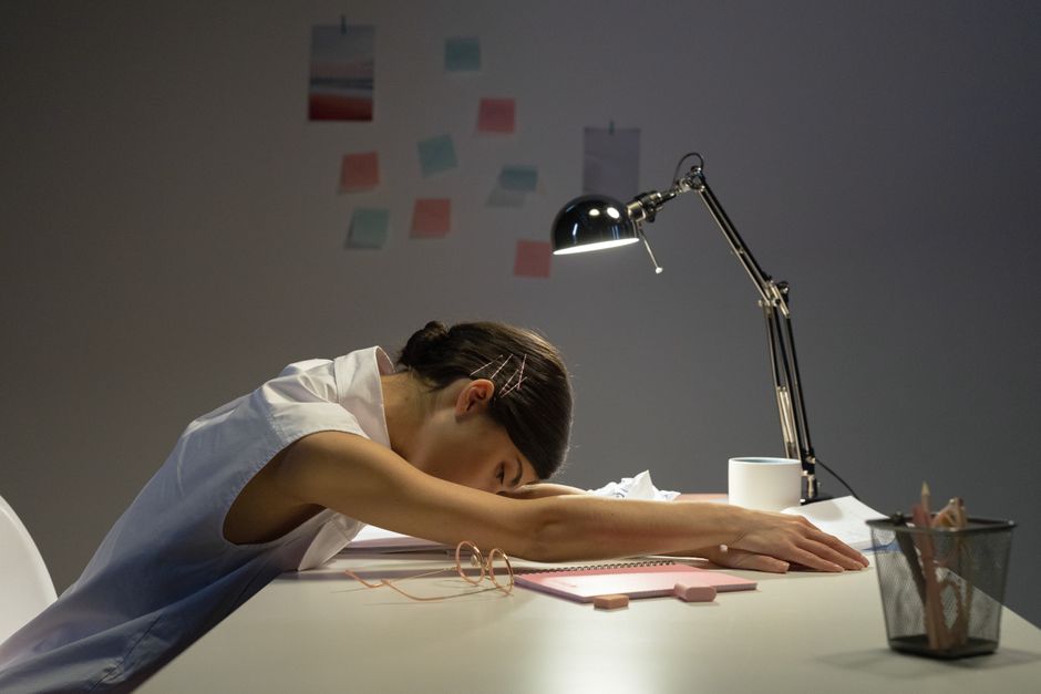 Pessoa exausta descansando sobre mesa de trabalho, refletindo cansaço e estresse no ambiente de escritório.